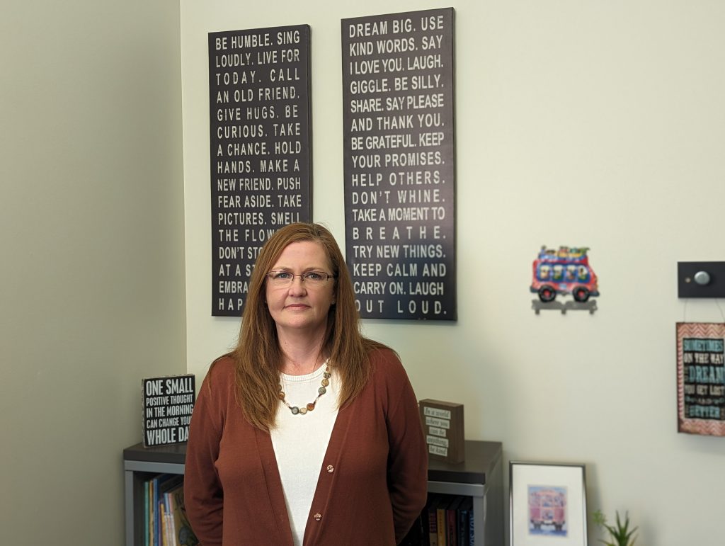 Photo of Summer Catino standing in her office with bookshelves and inspirational sign art behind her.