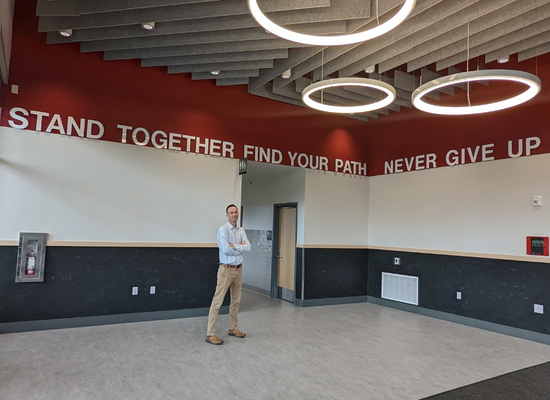 Todd Miller stands in the Santiam Middle/High School gym lobby under the school's maxims in large white lettering over a red wall: "Stand Together-Find Your Path-Never Give Up"