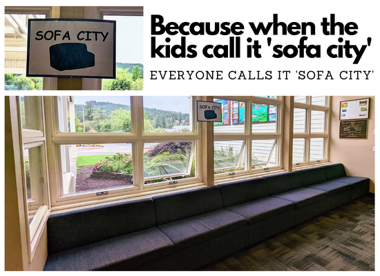Long dark blue bench sofa under large white wood framed windows with a sign above the seating that reads "sofa city"